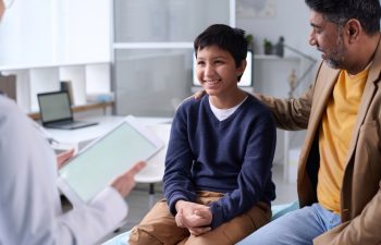 Portrait of smiling Middle Eastern boy visiting doctor in clinic with father supporting
